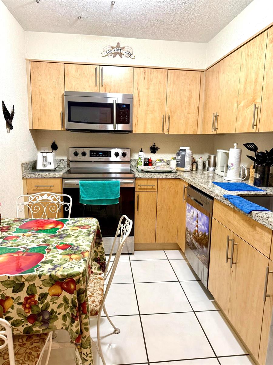A living room features a striped sofa with decorative pillows, a glass coffee table, and tile — 101 BRINY Avenue # 409, Pompano Beach FL 33062, POMPANO BEACH, FL