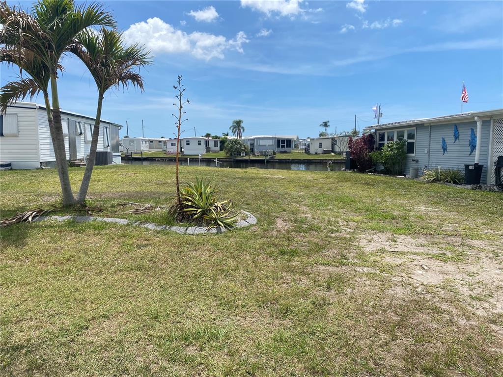 A grassy yard with a palm tree and landscaping overlooks a canal and mobile homes — 508 WINDSOR PLACE, NORTH PORT, FL