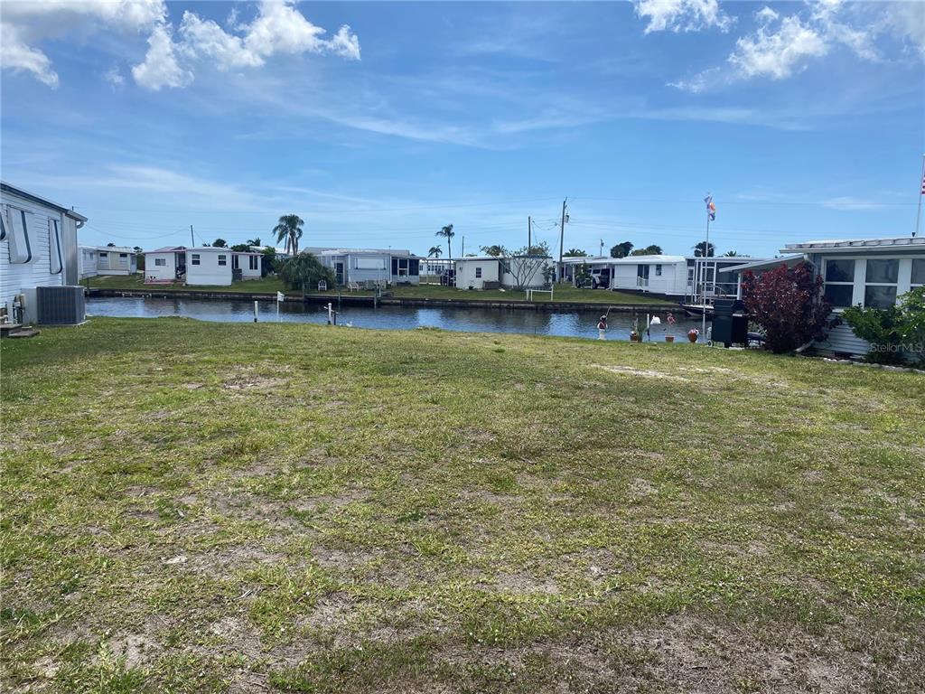 A grassy lot overlooks a narrow canal lined with mobile homes under a blue sky — 508 WINDSOR PLACE, NORTH PORT, FL
