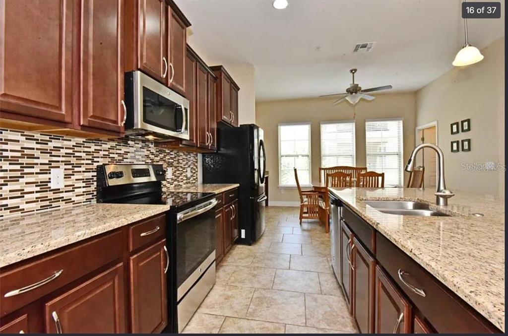 A kitchen features dark wood cabinets, granite countertops, a tiled backsplash, and stainless steel appliances — 3012 PORTA ROMANO WAY, LAKE MARY, FL