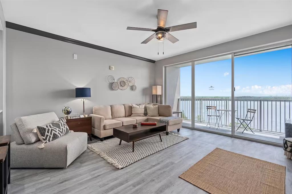 A living room with gray flooring, a sectional sofa, and a balcony overlooking the water — 13415 BLUE HERON BEACH DRIVE UNIT 706, ORLANDO, FL