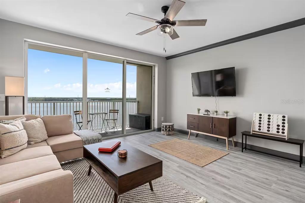 A living room with a sectional sofa, coffee table, wall-mounted television, and a balcony view — 13415 BLUE HERON BEACH DRIVE UNIT 706, ORLANDO, FL