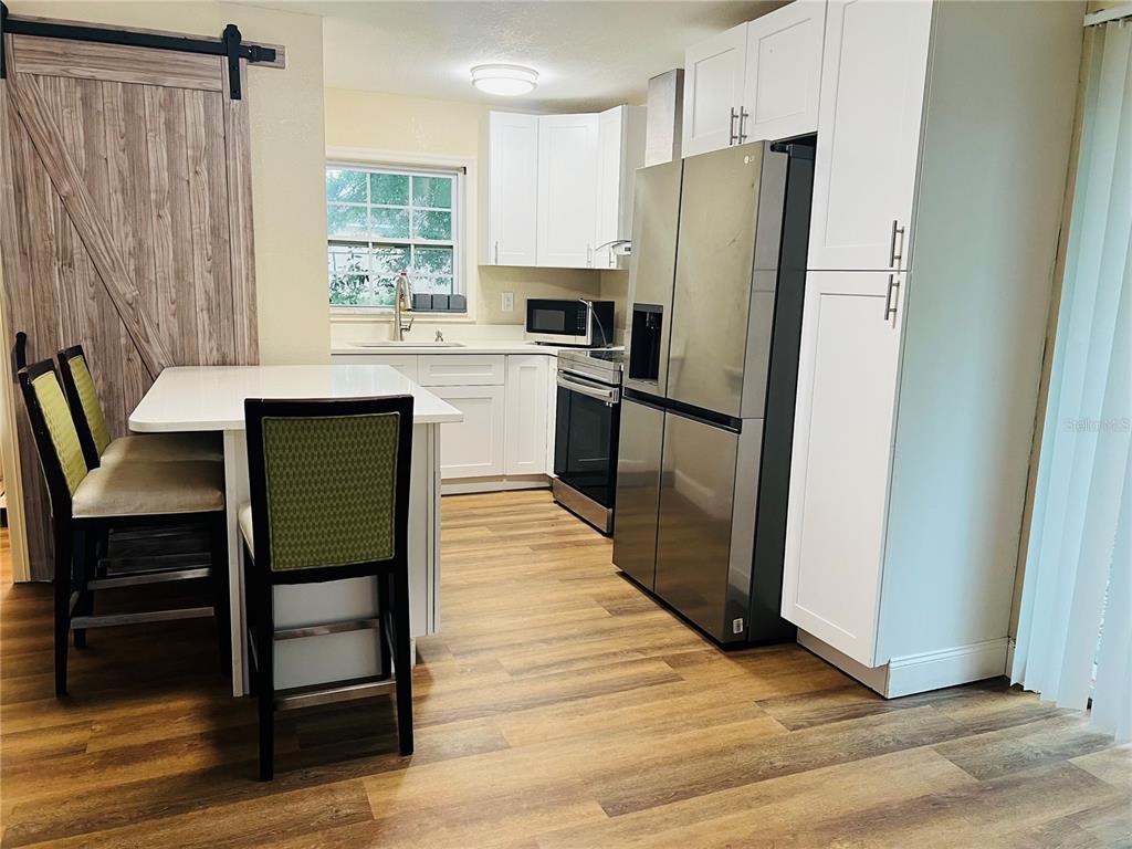 A kitchen features white cabinets, stainless steel appliances, a dining island, and wood-look flooring — 1218 KINGSTON AVENUE, ORLANDO, FL