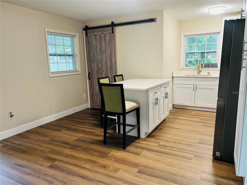 A kitchen features white cabinets, a central island with seating, and a sliding barn door — 1218 KINGSTON AVENUE, ORLANDO, FL