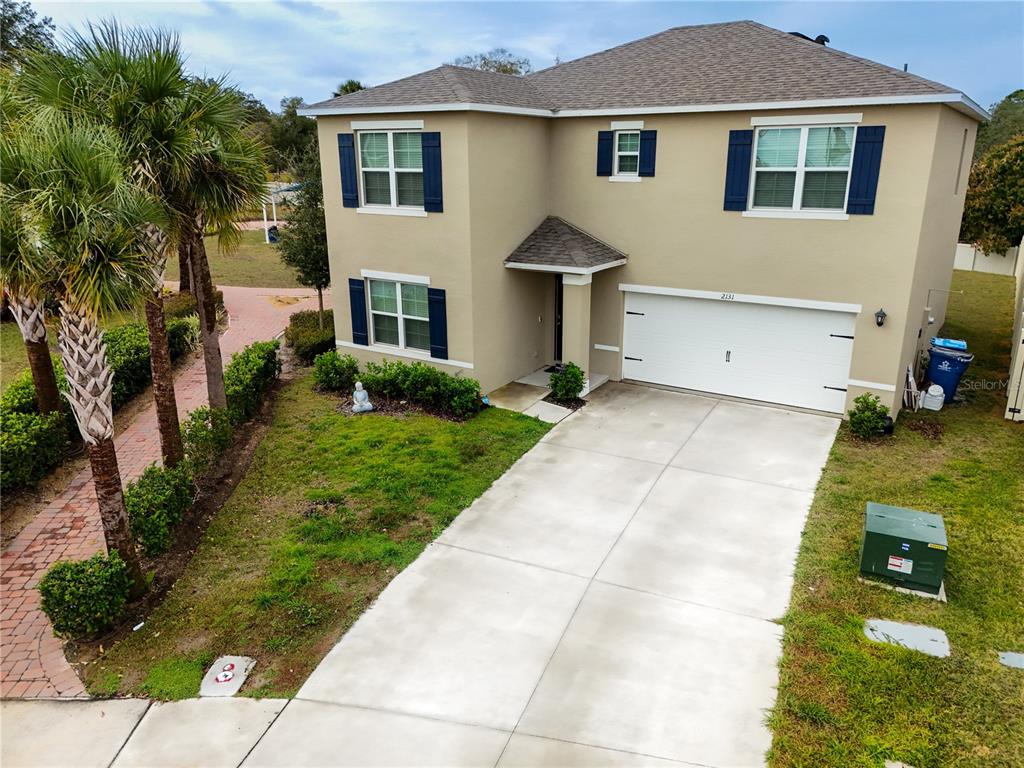 A two-story suburban house with a tan exterior, blue shutters, and a two-car garage — 2131 DOE RUN DRIVE, DAVENPORT, FL