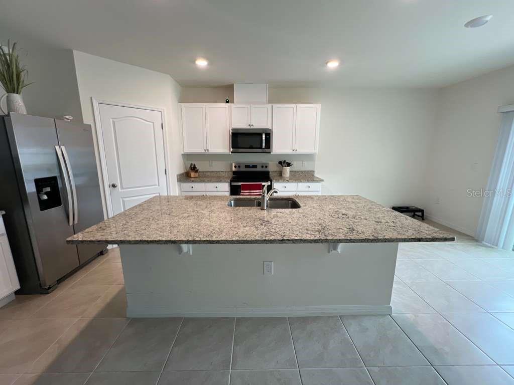 A kitchen features white cabinets, stainless steel appliances, and a large granite-topped island — 2131 DOE RUN DRIVE, DAVENPORT, FL