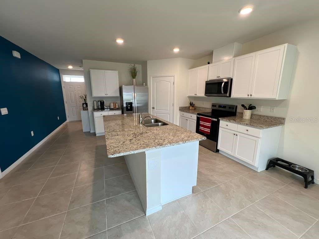 A kitchen features white cabinets, granite countertops, a center island, and a dark blue wall — 2131 DOE RUN DRIVE, DAVENPORT, FL