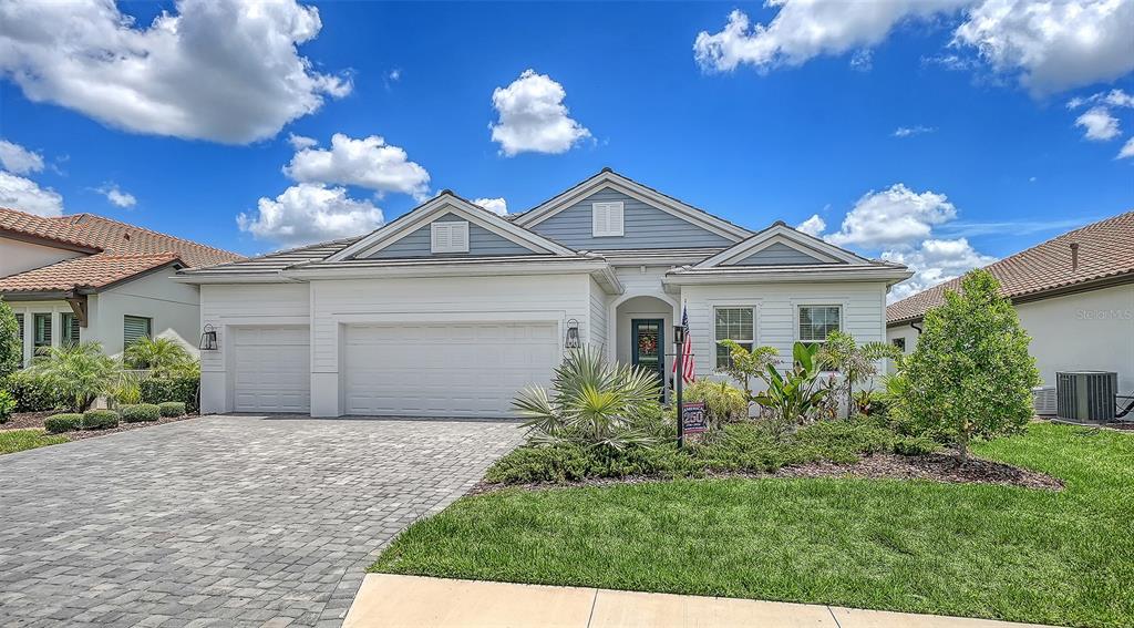 A single-story suburban house features a white exterior, a paved driveway, and a three-car garage — 13509 DEEP BLUE PLACE, BRADENTON, FL