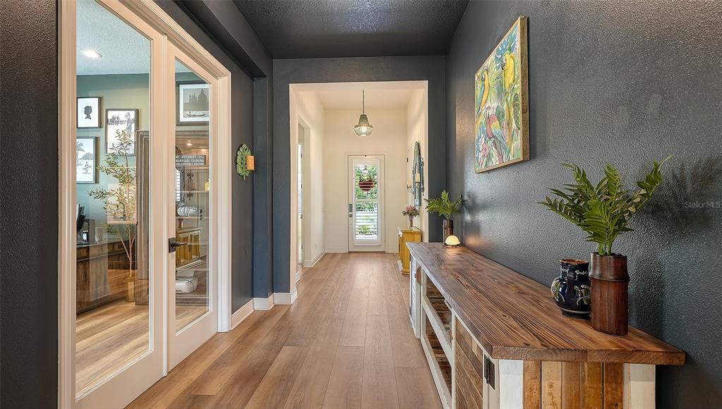 A hallway with dark walls, light wood flooring, a wooden console table, and glass-paned doors — 13509 DEEP BLUE PLACE, BRADENTON, FL