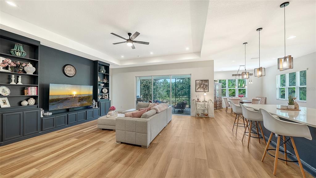 An open-concept living room and kitchen feature dark built-in shelving, light wood flooring, and island seating — 13509 DEEP BLUE PLACE, BRADENTON, FL