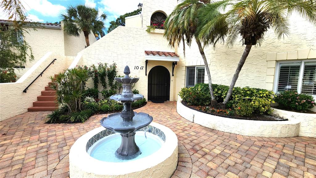 A tiered stone fountain sits in a paved courtyard before a stucco building entrance — 6101 34TH STREET W UNIT 10A, BRADENTON, FL