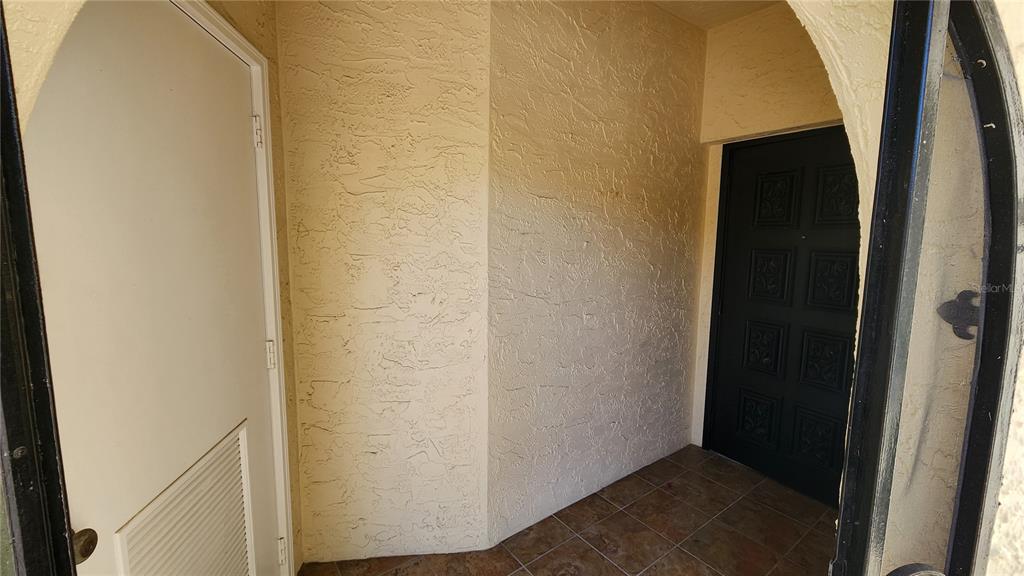A covered entryway features a textured beige wall, tiled floor, and a dark front door — 6101 34TH STREET W UNIT 10A, BRADENTON, FL