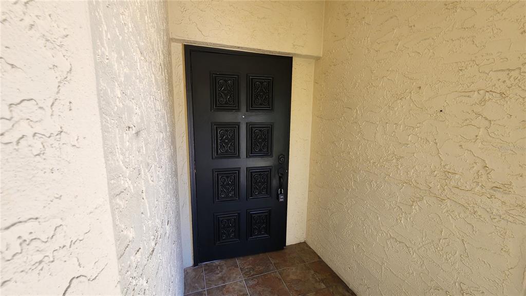 A black front door with eight rectangular panels is set in a textured stucco entryway — 6101 34TH STREET W UNIT 10A, BRADENTON, FL