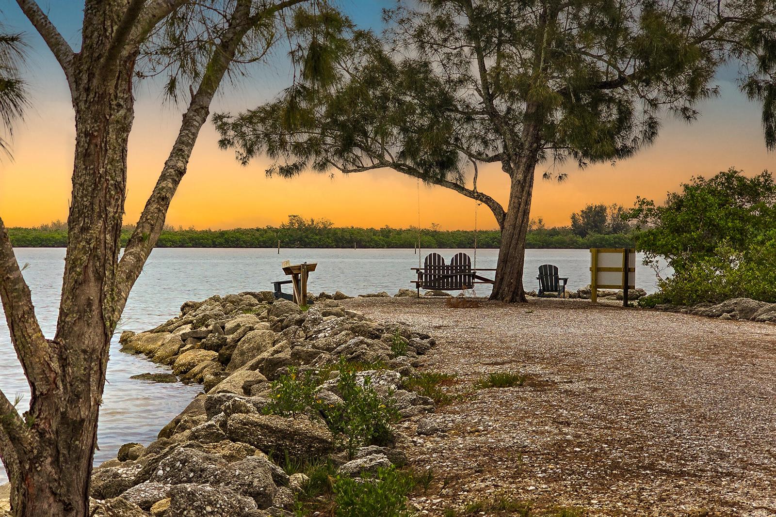 A gravel path leads to a waterfront area with a wooden swing and Adirondack chairs — 3586 Lucia Drive, Vero Beach FL 32967, VERO BEACH, FL