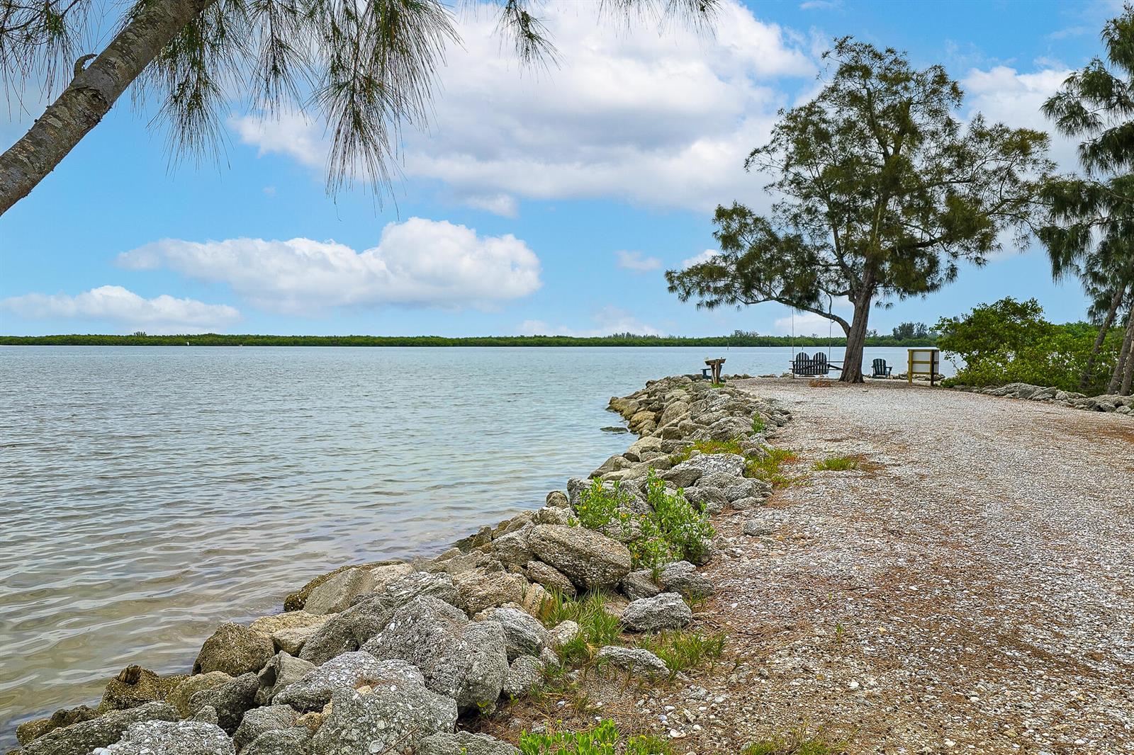 A rocky shoreline borders a calm body of water with a tree and seating area — 3586 Lucia Drive, Vero Beach FL 32967, VERO BEACH, FL