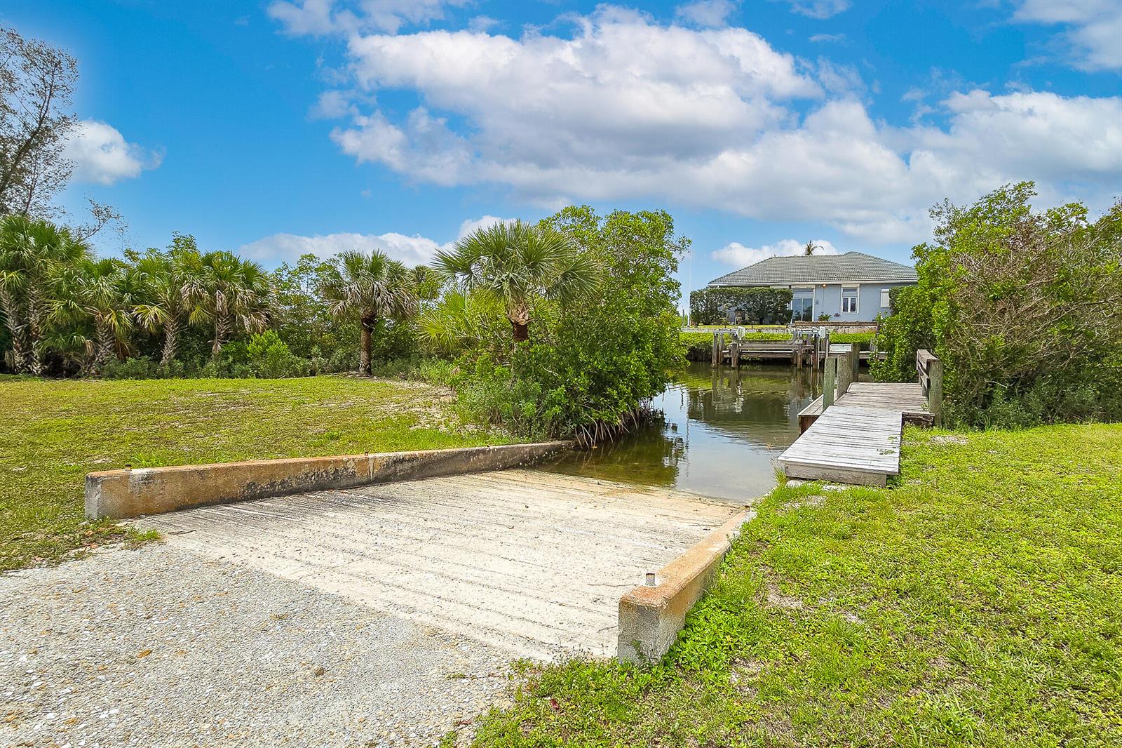 A concrete boat ramp leads into a narrow canal next to a wooden dock — 3586 Lucia Drive, Vero Beach FL 32967, VERO BEACH, FL
