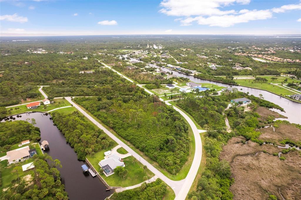 An aerial view shows a house with a pool cage along a canal and woods — 12518 EISENHOWER DRIVE, PORT CHARLOTTE, FL