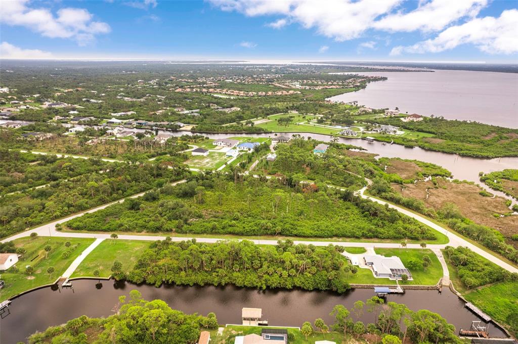 An aerial view shows a waterfront property with a canal, lush vegetation, and nearby homes — 12518 EISENHOWER DRIVE, PORT CHARLOTTE, FL