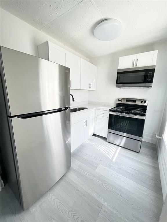 A kitchen features stainless steel appliances, white cabinetry, and light wood-look flooring — 205 S GROVE STREET, EUSTIS, FL
