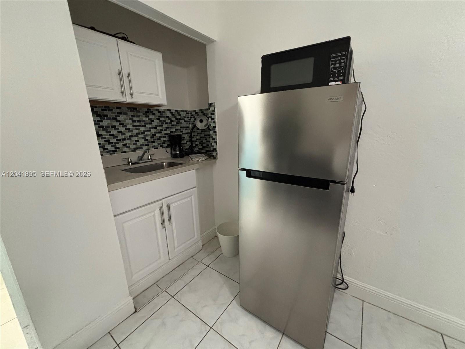 A small kitchenette features white cabinets, a stainless steel refrigerator, and a tiled backsplash — 1843 Dewey St # 118, Hollywood FL 33020, HOLLYWOOD, FL