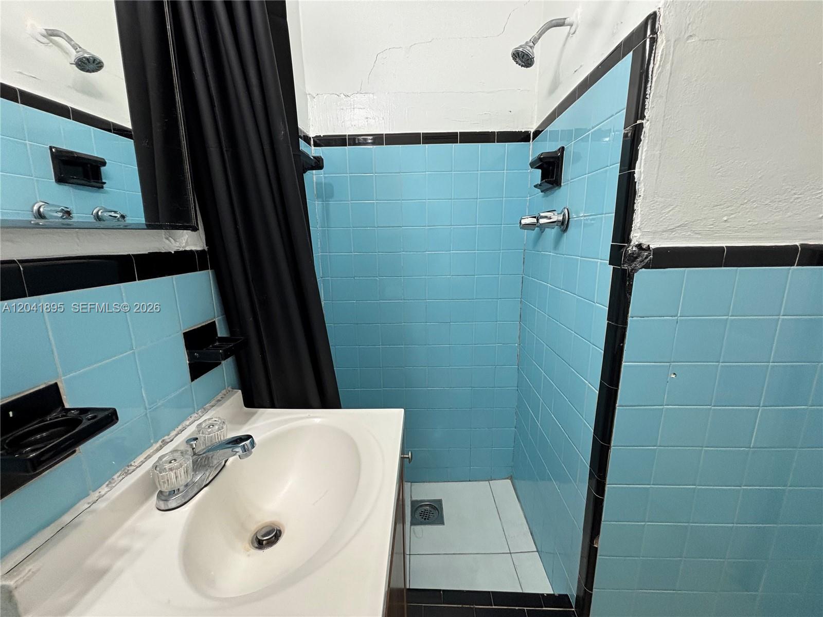 A bathroom features a vanity, a shower stall with blue tiles, and black trim — 1843 Dewey St # 118, Hollywood FL 33020, HOLLYWOOD, FL