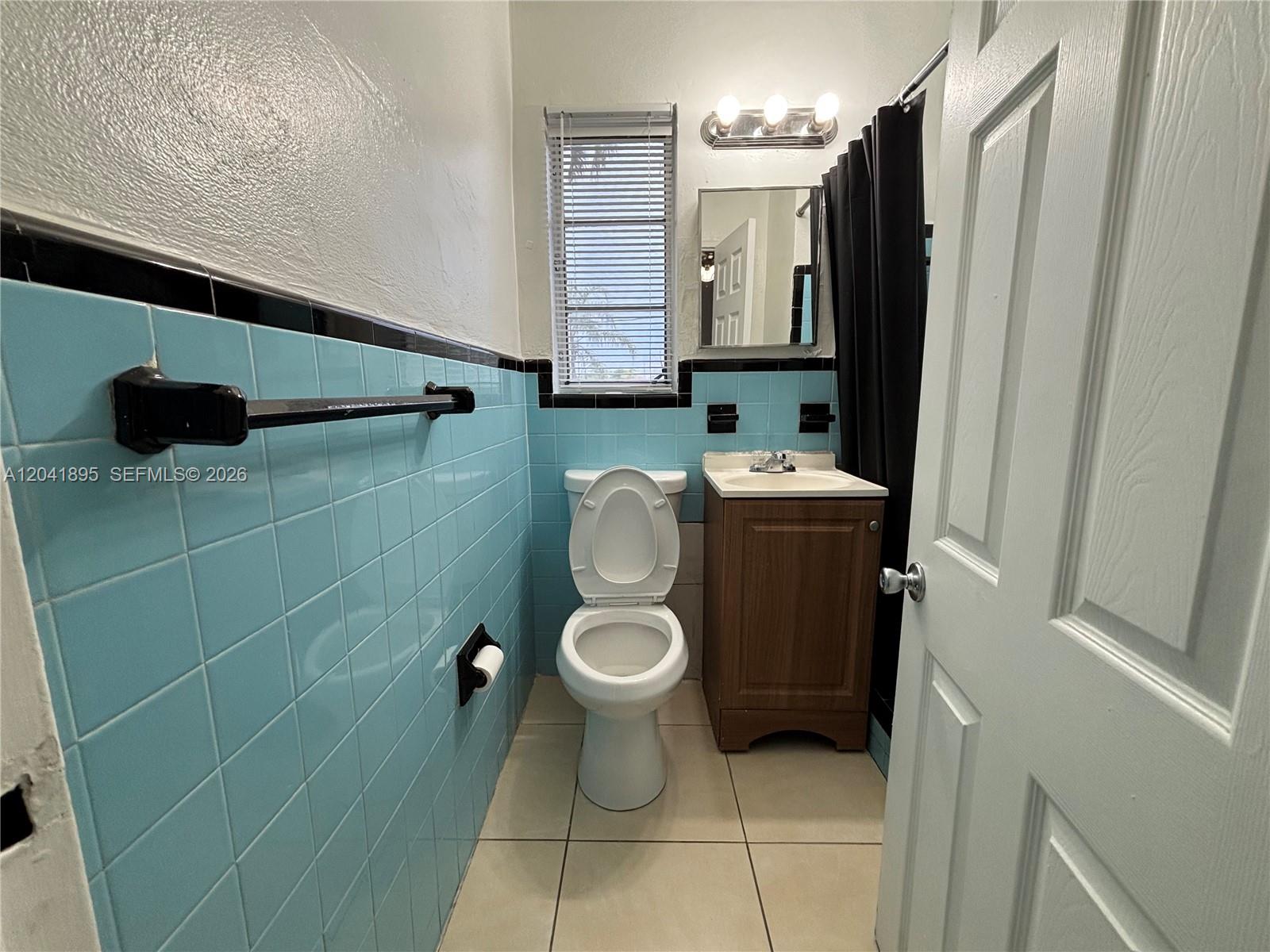A bathroom features light blue wall tiles, a black accent border, and a wood vanity — 1843 Dewey St # 118, Hollywood FL 33020, HOLLYWOOD, FL
