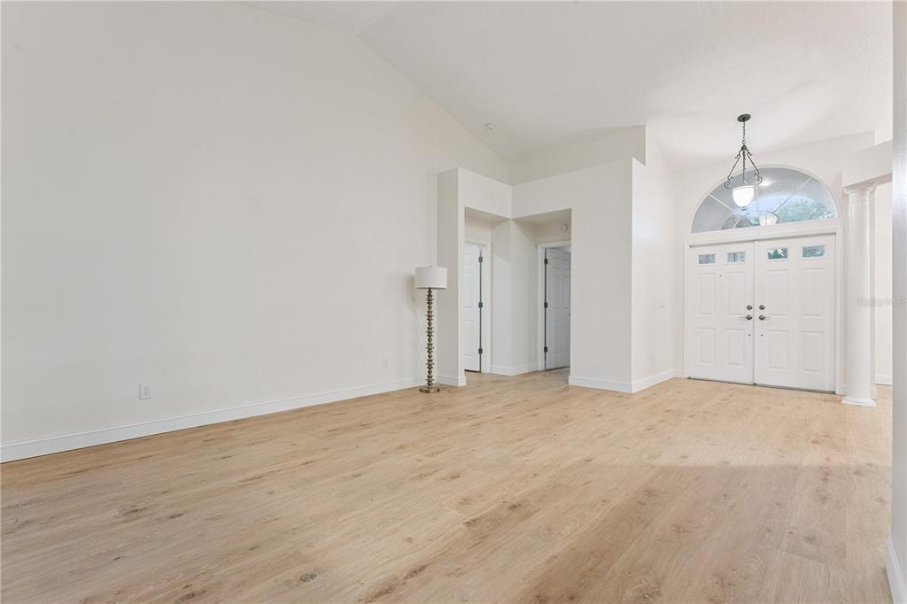An empty room with light wood-look flooring, white walls, vaulted ceilings, and a double-door entryway — 14962 FAVERSHAM CIRCLE, ORLANDO, FL