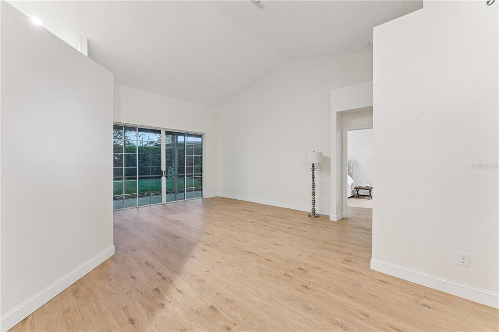 An empty room with light wood-look flooring, vaulted ceilings, and sliding glass doors to a yard — 14962 FAVERSHAM CIRCLE, ORLANDO, FL