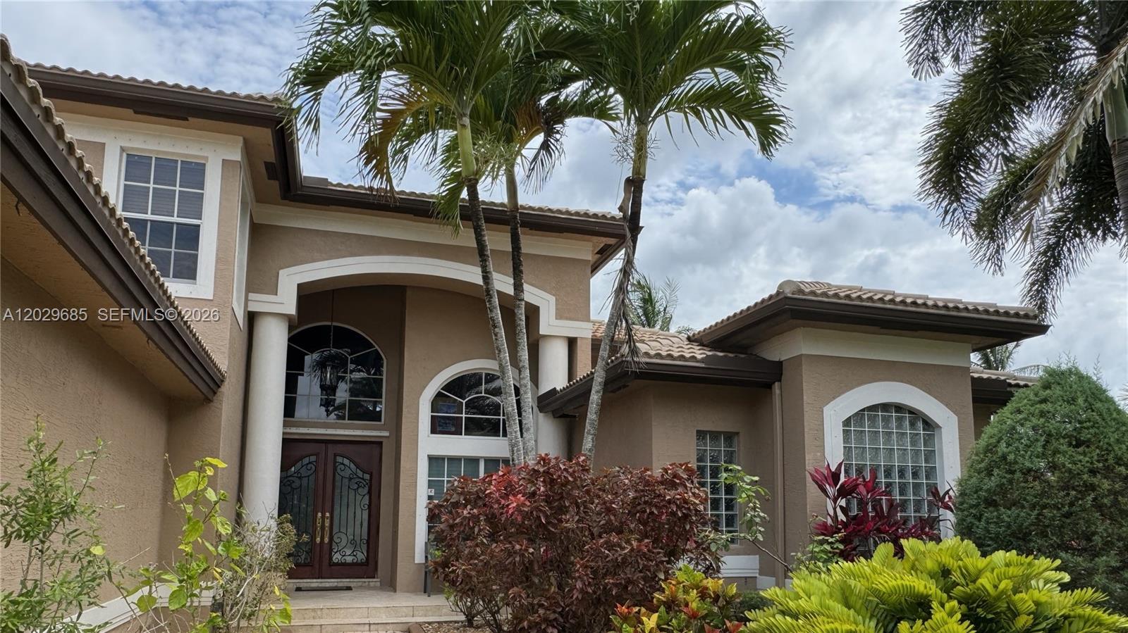 The exterior of a tan stucco house features a double-door entrance and arched windows — 10445 Canterbury Ct, Davie FL 33328, DAVIE, FL