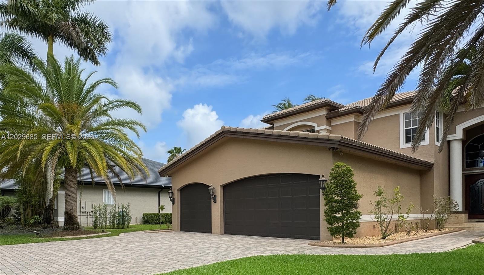 A beige two-story house features a three-car garage and a paved driveway with palm trees — 10445 Canterbury Ct, Davie FL 33328, DAVIE, FL