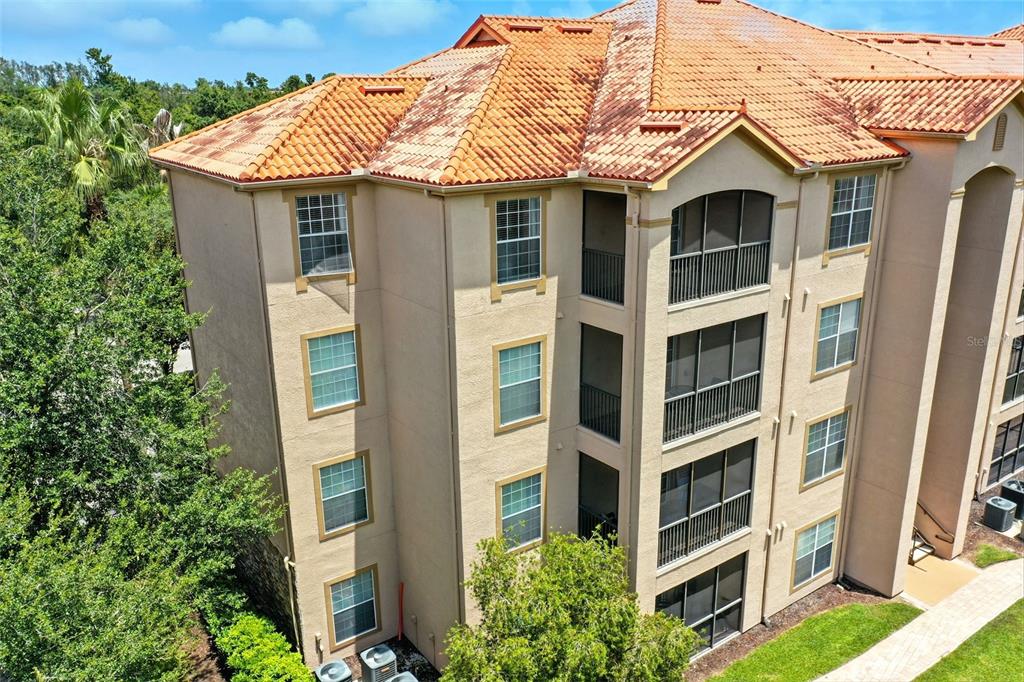 An exterior view of a multi-story apartment building with a tiled roof and screened balconies — 8010 TUSCANY WAY UNIT 5206, DAVENPORT, FL