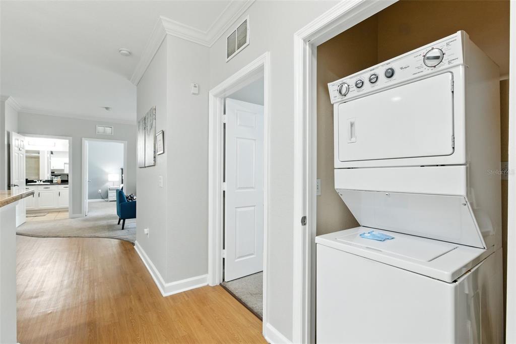 A hallway with wood-look flooring leads to a bedroom and bathroom, featuring a stacked laundry unit — 8010 TUSCANY WAY UNIT 5206, DAVENPORT, FL