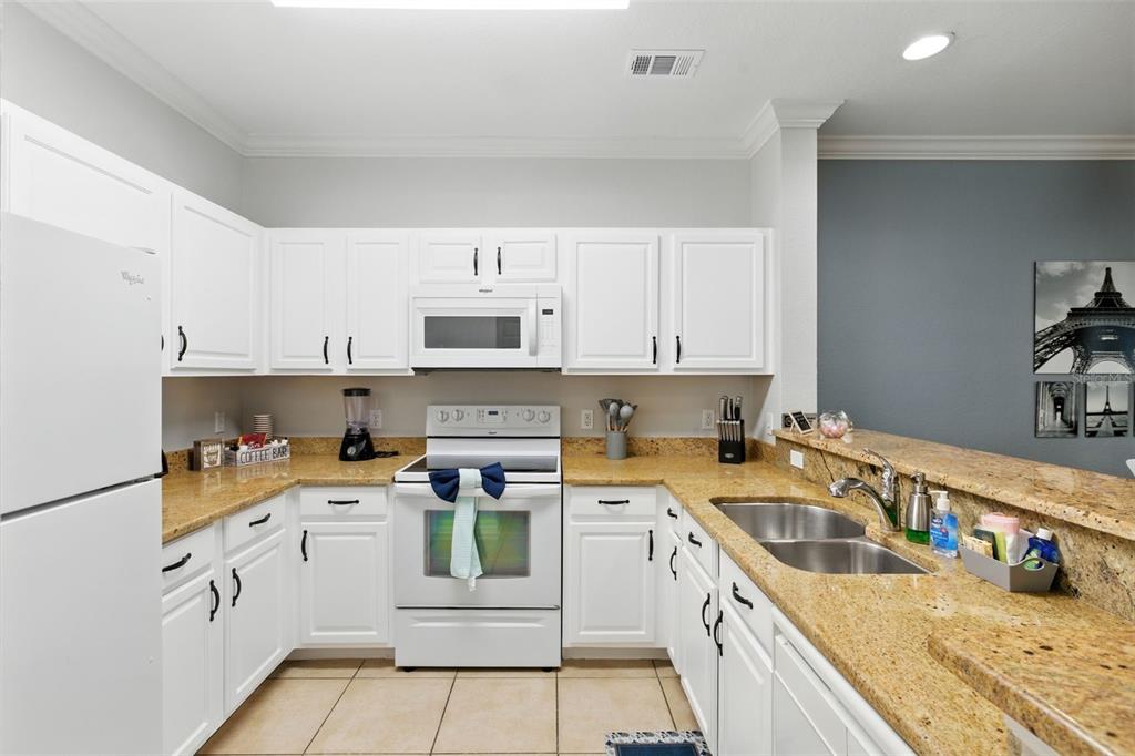 A kitchen with white cabinets, granite countertops, stainless steel sink, and white appliances — 8010 TUSCANY WAY UNIT 5206, DAVENPORT, FL