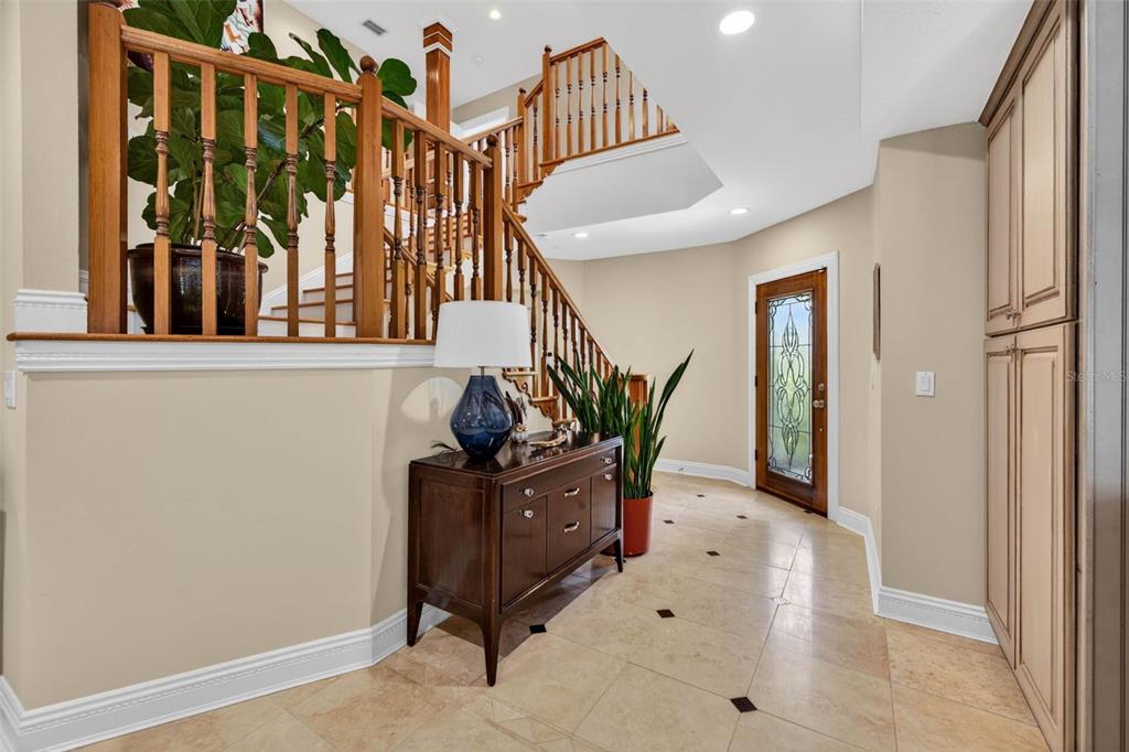 A foyer features a wooden staircase, tile flooring, a dark wood console table, and plants — 342 2ND AVENUE N, TIERRA VERDE, FL