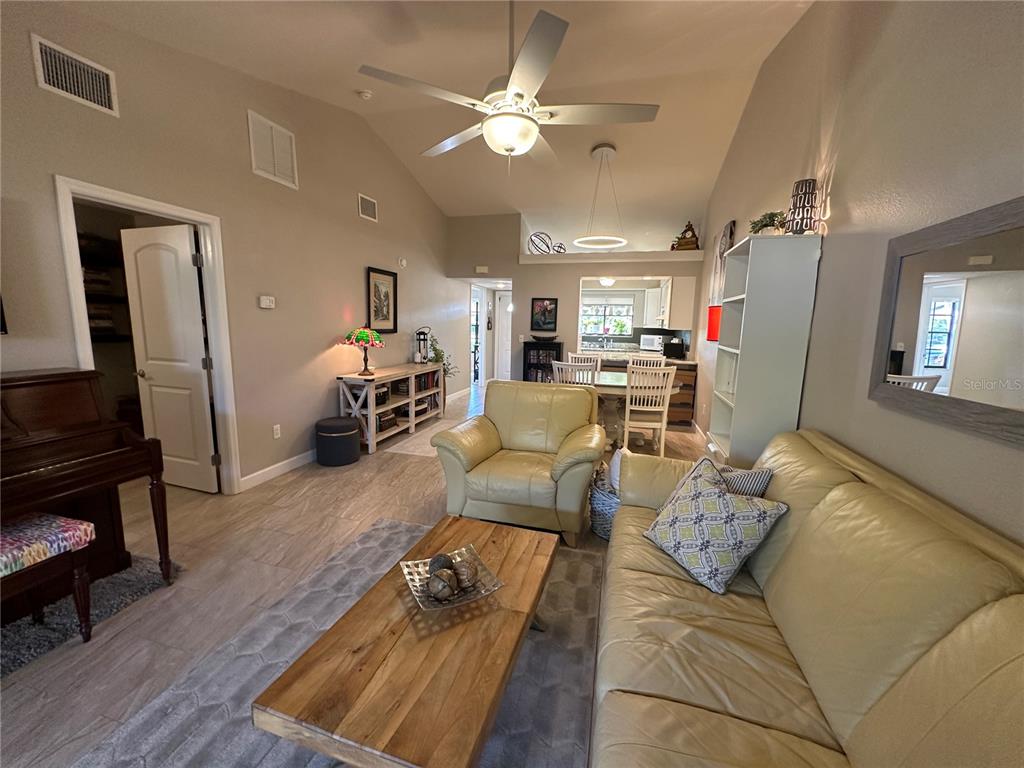 A living room features a vaulted ceiling, light-colored tile flooring, and a beige leather sofa — 5480 BRASSY LOOP, NORTH PORT, FL
