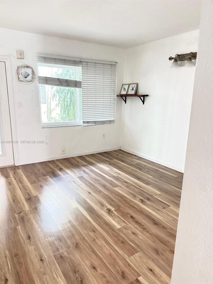 An empty room features wood-look laminate flooring, a window with blinds, and a wall shelf — 655 Meridian Ave # 2, Miami Beach FL 33139, MIAMI BEACH, FL