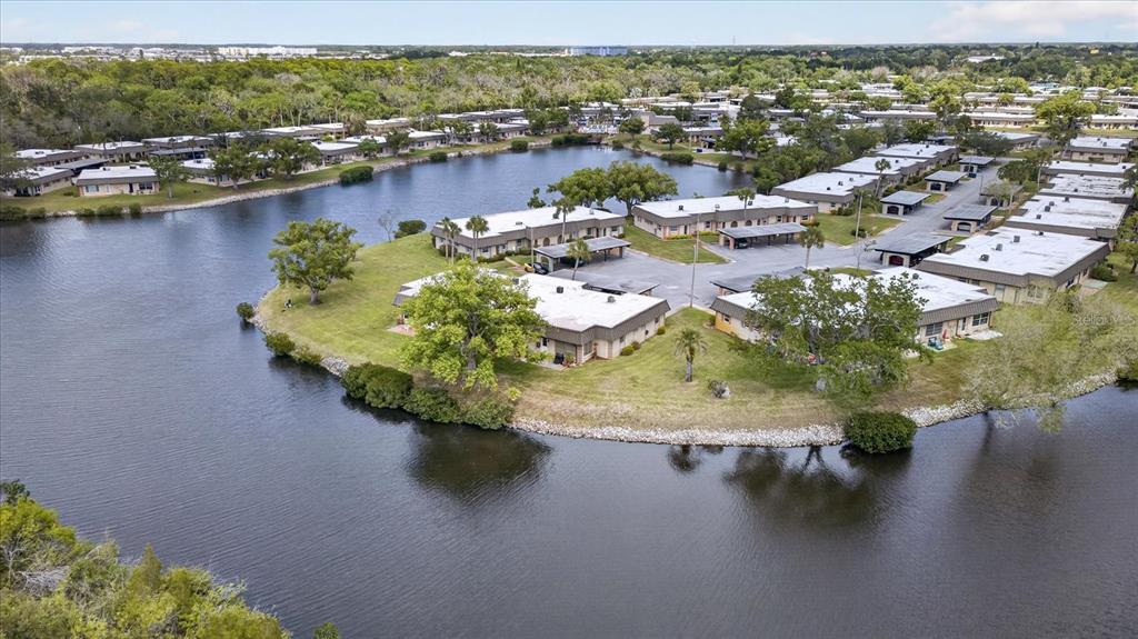 An aerial view shows several single-story apartment buildings situated on a grassy peninsula surrounded by water — 4116 HAMPTON DRIVE, NEW PORT RICHEY, FL
