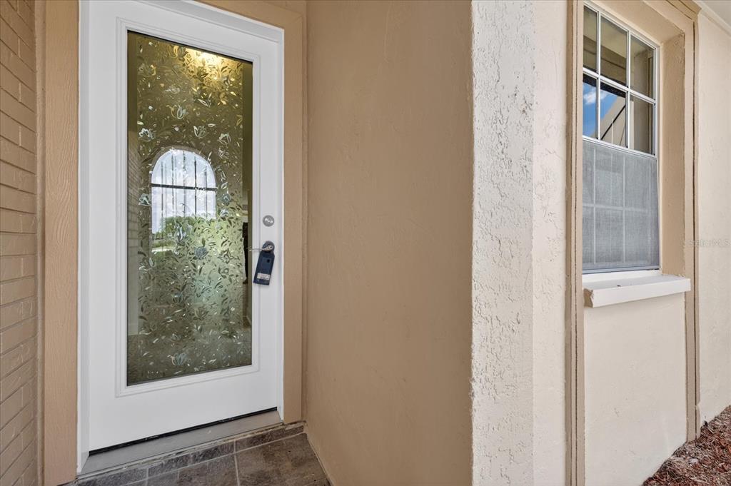 A white front door with a decorative glass insert sits beside a window with shutters — 4116 HAMPTON DRIVE, NEW PORT RICHEY, FL