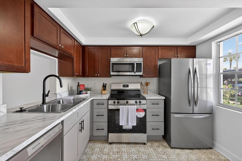 A kitchen features dark wood upper cabinets, light gray lower cabinets, stainless steel appliances, and countertops — 4116 HAMPTON DRIVE, NEW PORT RICHEY, FL