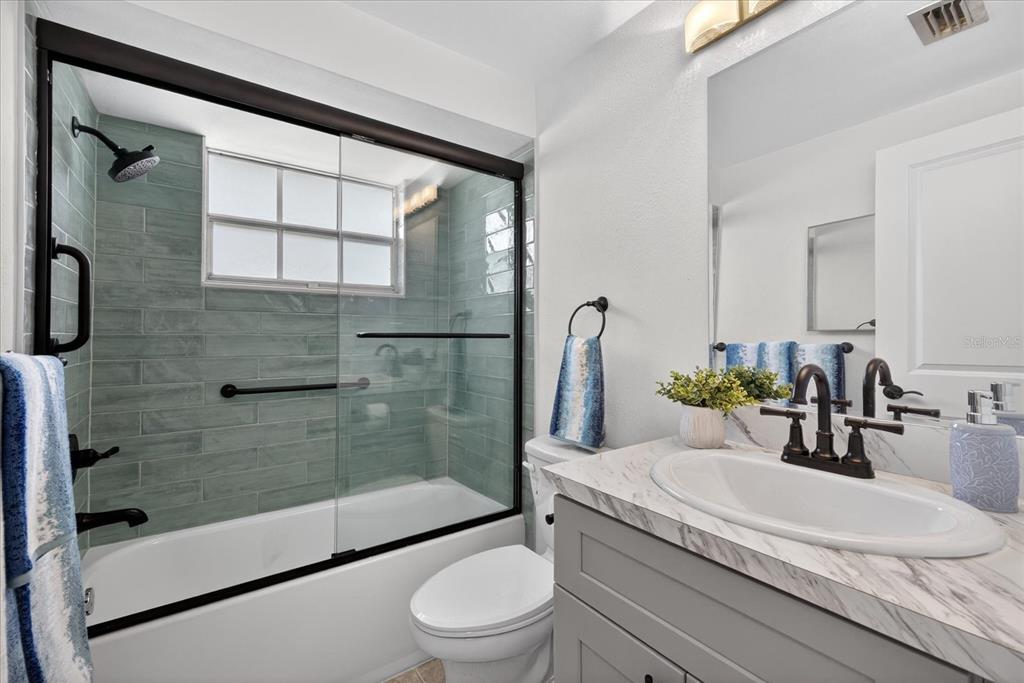 A bathroom features a gray vanity, a marble-look countertop, and a tiled shower-tub combination — 4116 HAMPTON DRIVE, NEW PORT RICHEY, FL