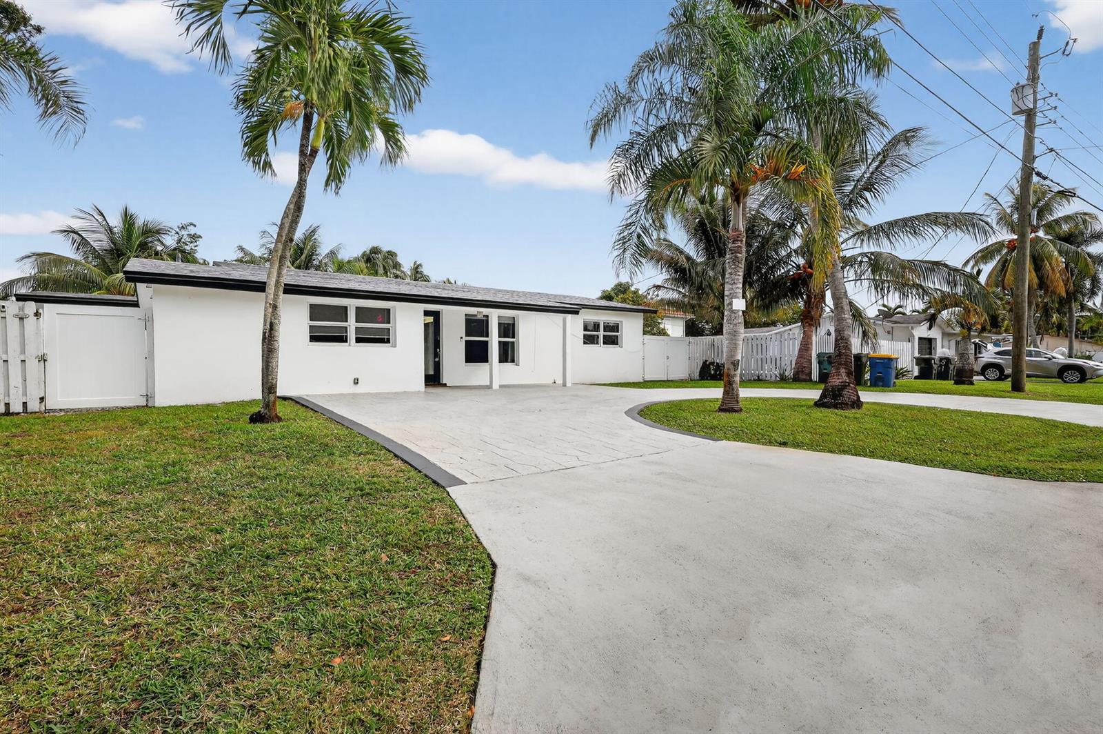 A white, single-story house features a concrete driveway, palm trees, and a white fence — 4540 SW 28th Terrace, Dania Beach FL 33312, DANIA BEACH, FL