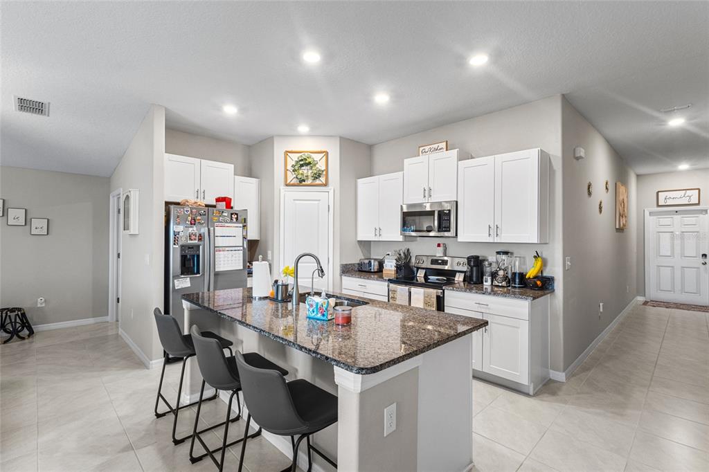 A kitchen features white cabinets, granite countertops, a central island with bar seating, and tile flooring — 5426 BLUE AZURE DRIVE, WIMAUMA, FL