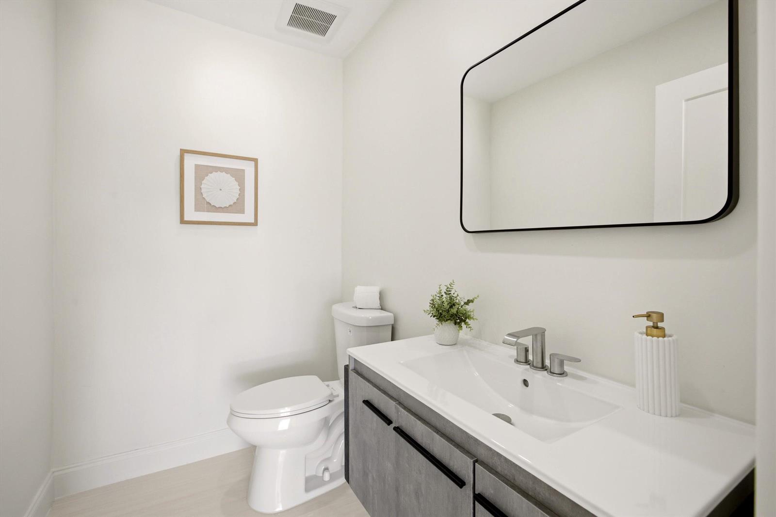 A modern powder room features a gray vanity, a white countertop, and a rectangular mirror — 401 NW 3rd Place, Dania Beach FL 33004, DANIA BEACH, FL