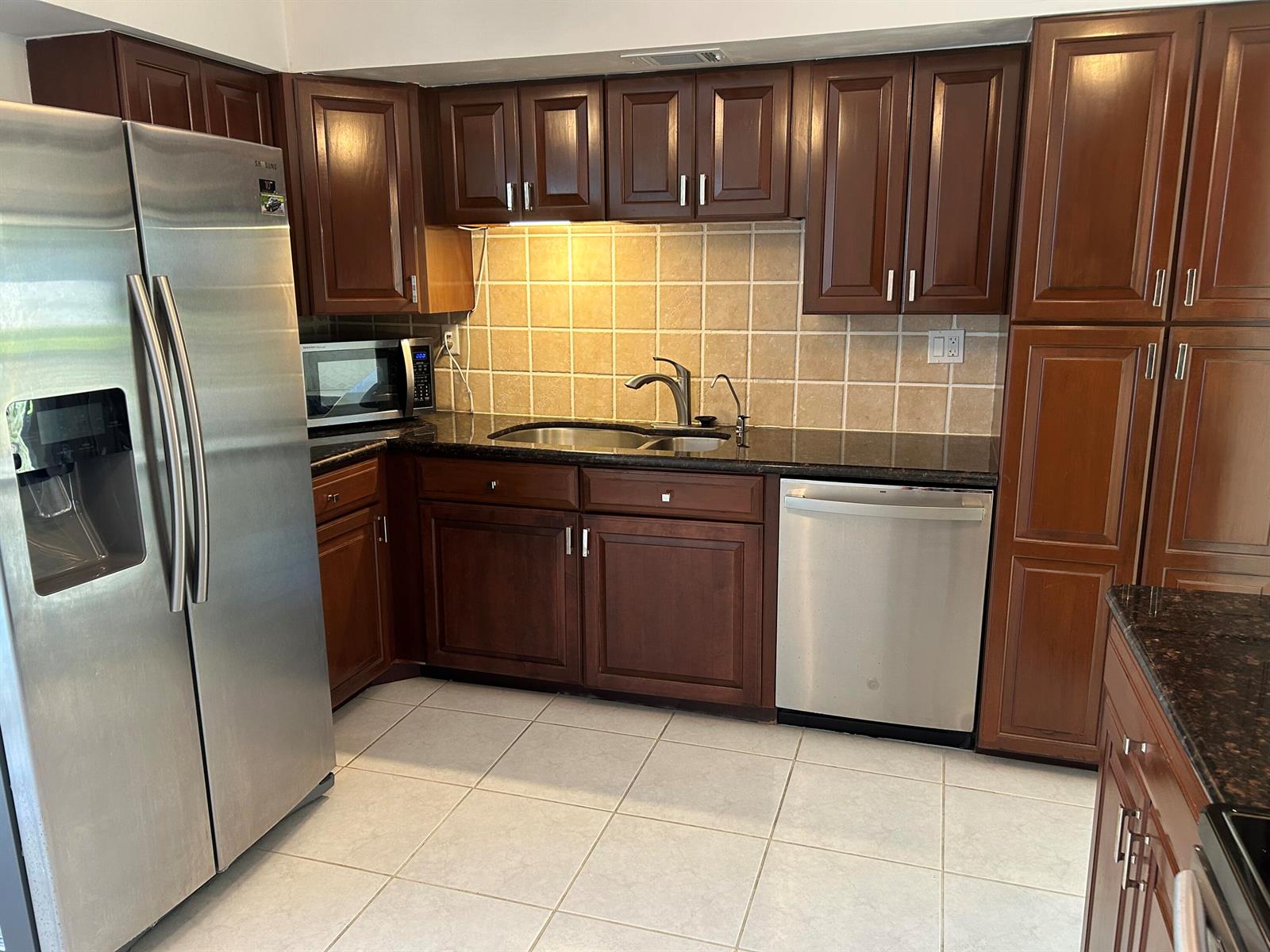 A kitchen features dark wood cabinets, stainless steel appliances, a tiled backsplash, and granite countertops — 6514 Spring Bottom Way # 125, Boca Raton FL 33433, BOCA RATON, FL