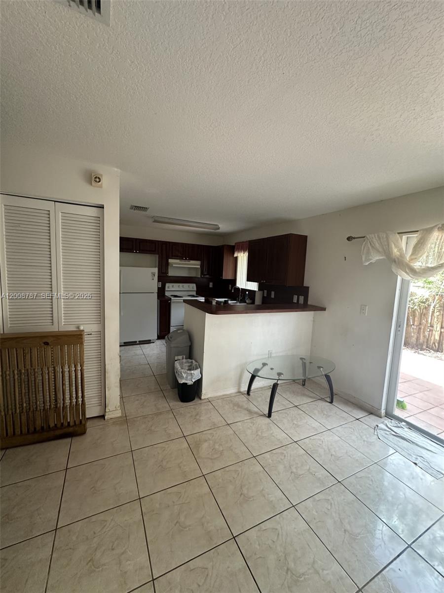 A kitchen with dark wood cabinets and tile flooring opens to a dining area — 7125 NW 173rd Dr # 2401, Hialeah FL 33015, HIALEAH, FL