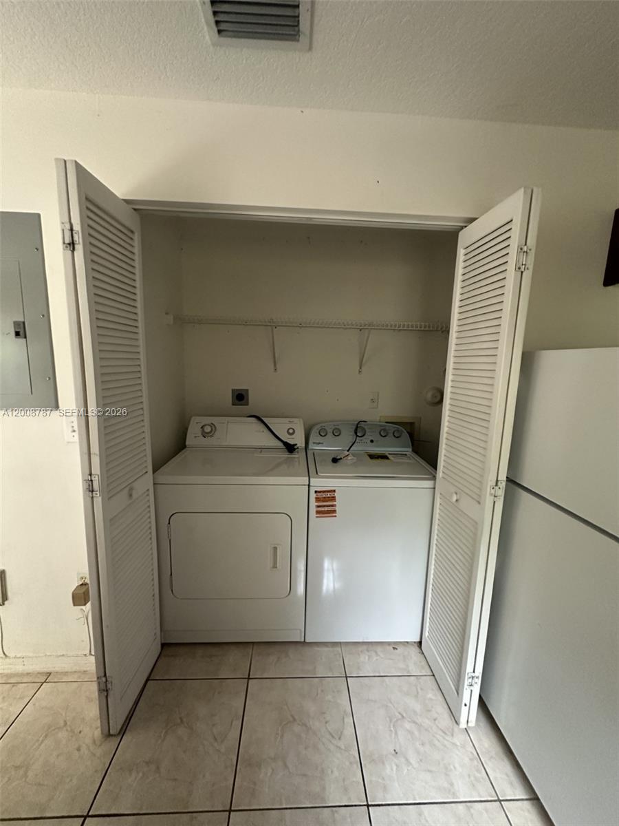 A laundry closet contains a white washer and dryer set on a tiled floor — 7125 NW 173rd Dr # 2401, Hialeah FL 33015, HIALEAH, FL