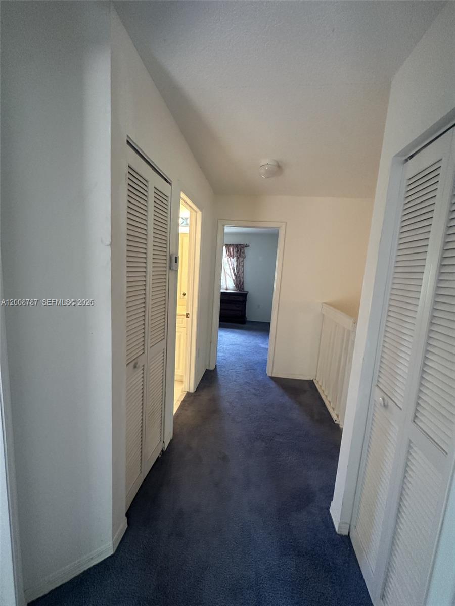 A hallway with blue carpeting features louvered closet doors and leads to a bedroom — 7125 NW 173rd Dr # 2401, Hialeah FL 33015, HIALEAH, FL