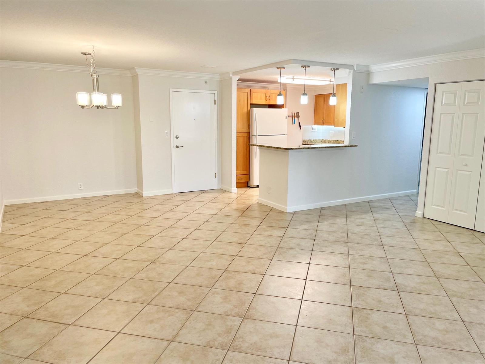 An open-concept living area features beige tile flooring, a dining chandelier, and a kitchen peninsula — 1000 Spanish River Road # 2n, Boca Raton FL 33432, BOCA RATON, FL