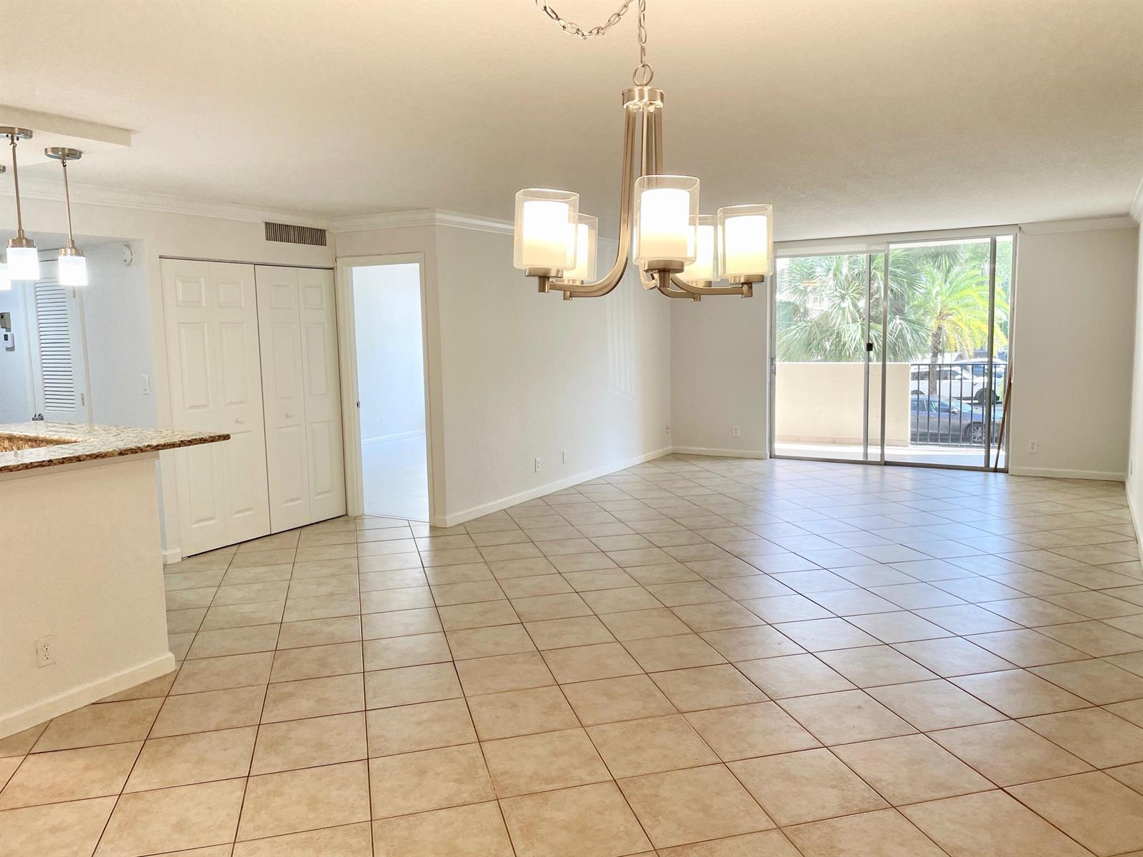 An open-concept living and dining area features tile flooring, a chandelier, and sliding glass doors — 1000 Spanish River Road # 2n, Boca Raton FL 33432, BOCA RATON, FL