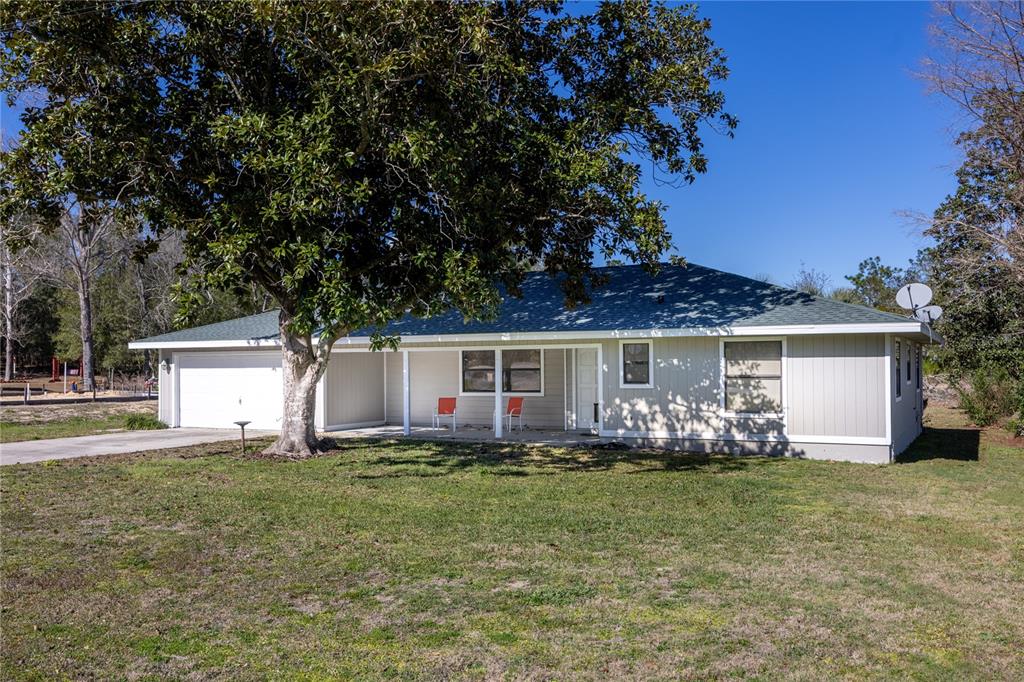 A single-story house with light-colored siding, a green roof, and a large front yard tree — 15181 NE 9TH STREET, WILLISTON, FL
